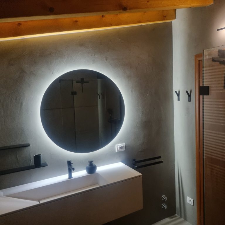 Badsanierung Gardasee Modernisiertes Badezimmer in einer Ferienimmobilie am Gardasee mit beleuchtetem Rundspiegel und Waschtisch