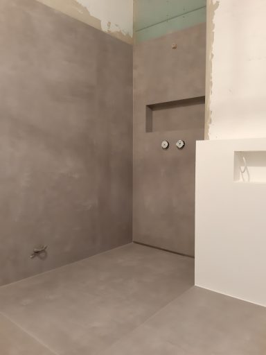 Dusche mit grauen Wänden und fliesenartigem Boden, unvollendeter Zustand.